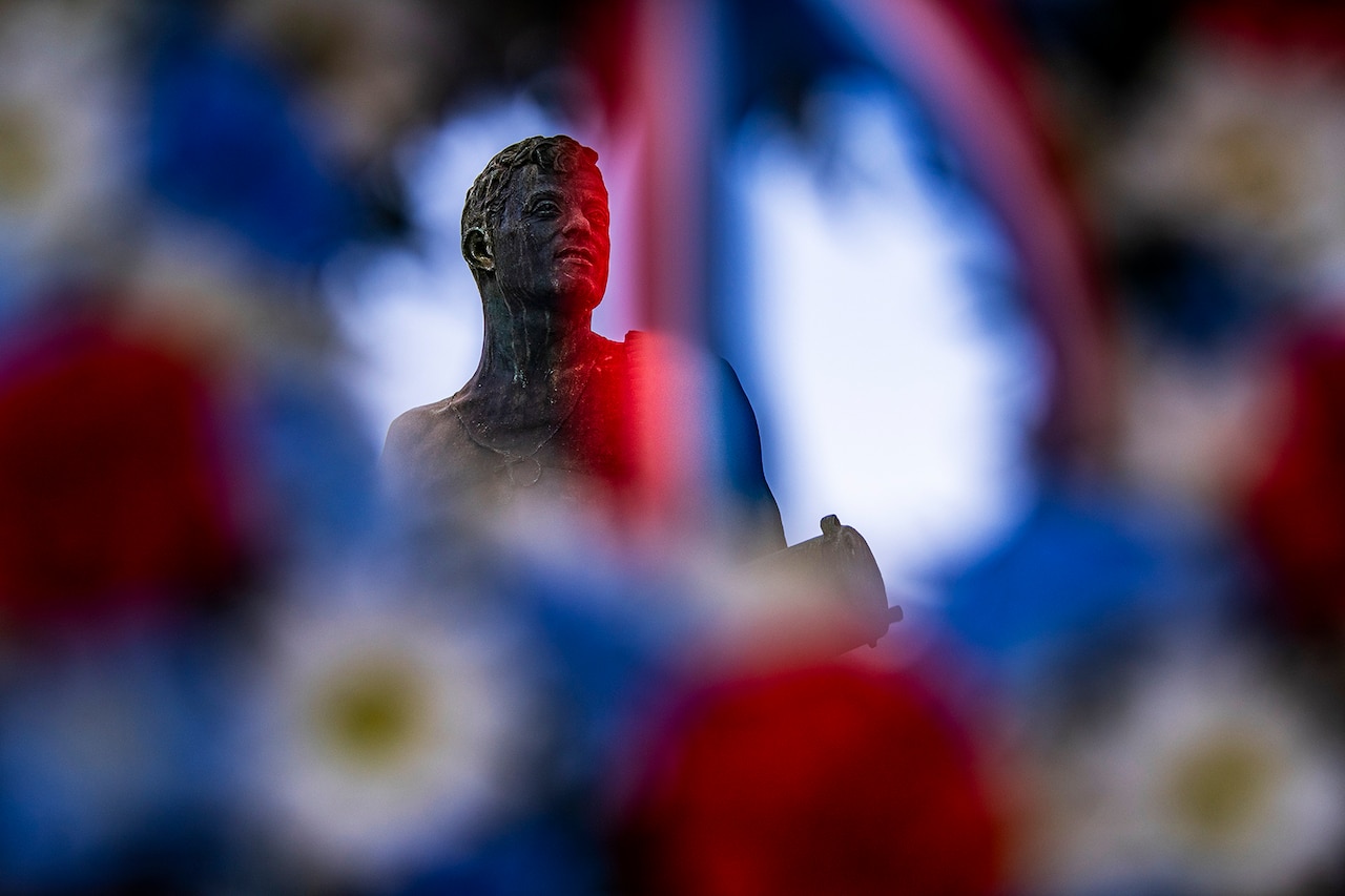 A statue is seen through the circle of a wreath.