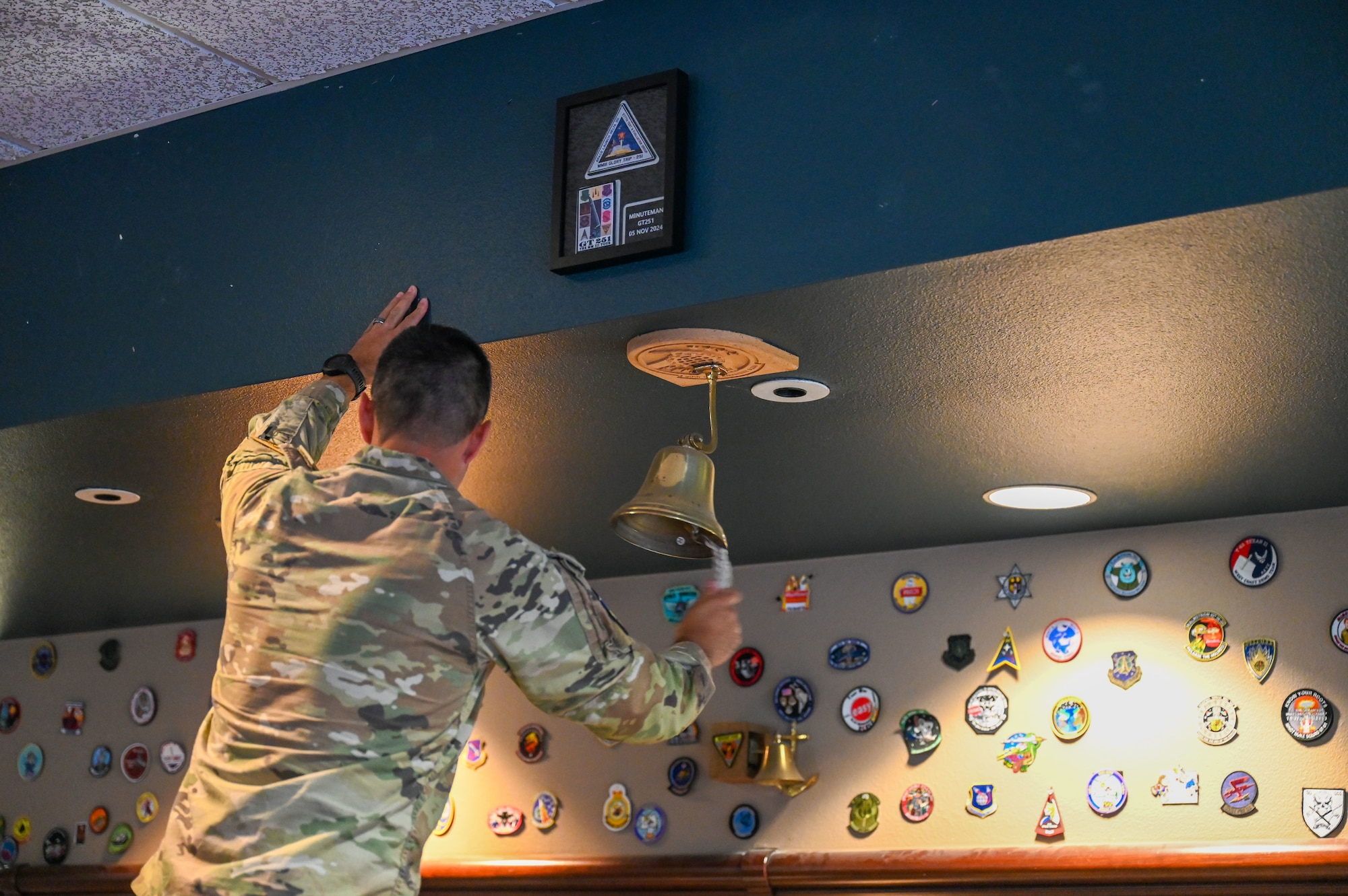 A man on a latter rings a bell hung from the ceiling.