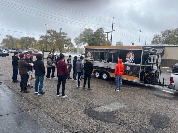 Airmen crown around and line up at a food truck in a parking lot.