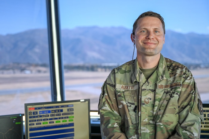 An Air Force airman poses in an air traffic control tower with mountains in background.