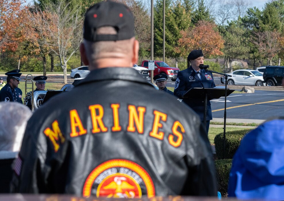 A man stands, with  his back to the camera, wearing a black jacket with the word "MARINES" in yellow across his shoulders and the USMC Globe and Eagle emblem below.