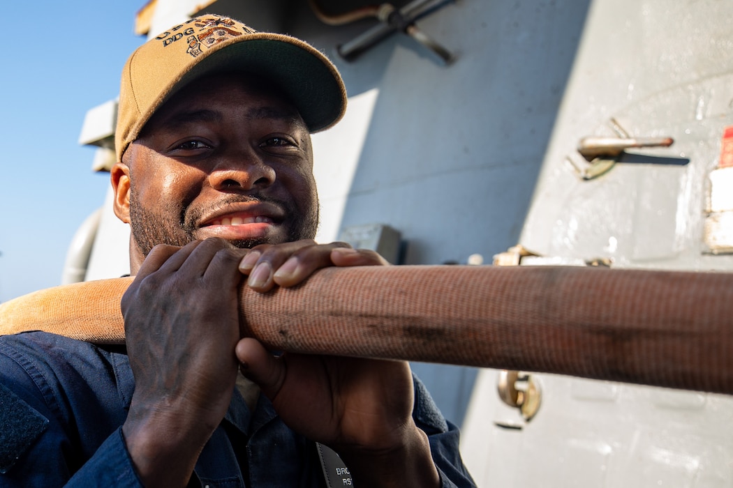 A U.S. Navy Retail Services Specialist mans a hose during a fresh water wash down aboard Arleigh Burke-class guided-missile destroyer USS Cole (DDG 67) in the U.S. Central Command area of responsibility.