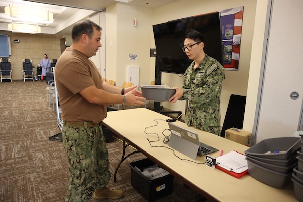 Petty Officer 2nd Class Daniel Kim (right), a laboratory technician corpsman from Naval Medical Center San Diego, hands Chief Petty Officer Richard Anderson, Expeditionary Medical Facility 150 Alpha’s operations chief, the items needed to move to the blood donation area during an Armed Services Blood Program – Camp Pendleton blood drive coordinated by the Navy Medicine Readiness and Training Command Camp Pendleton Junior Enlisted Association on Nov. 18, 2024, in the Naval Hospital Camp Pendleton Galley Meeting Room.