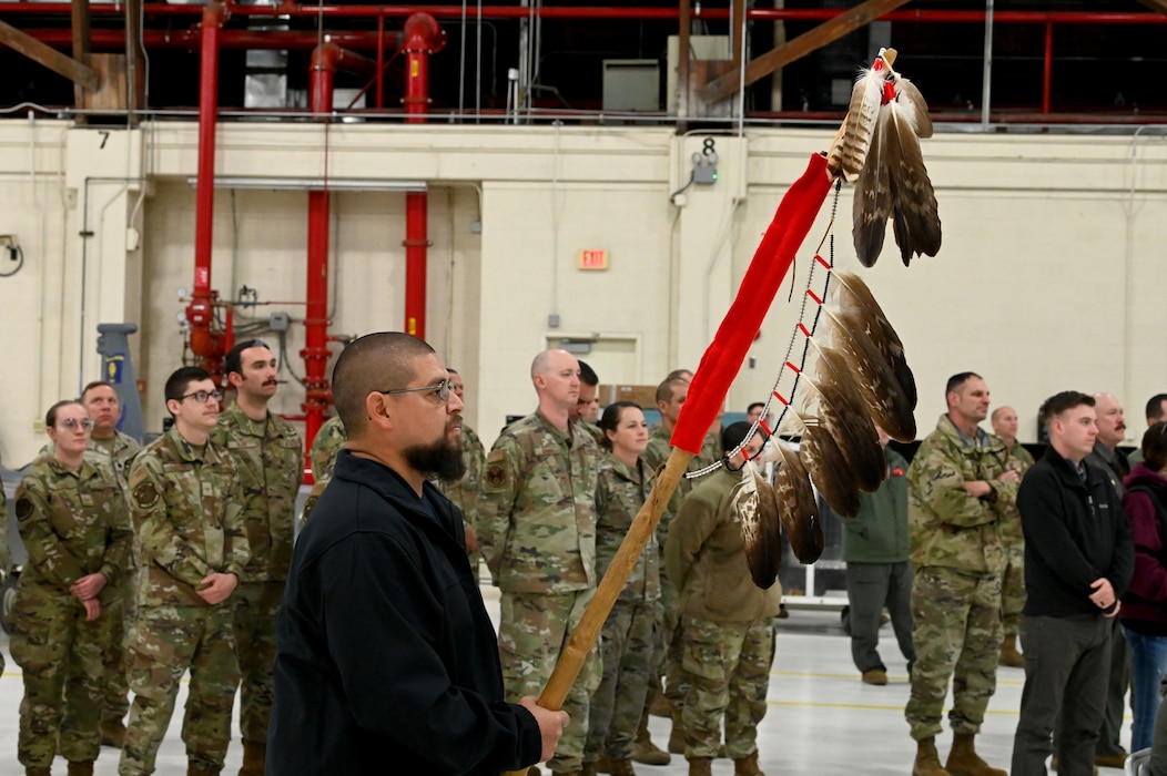 Person stands holding a staff with eagle feathers.