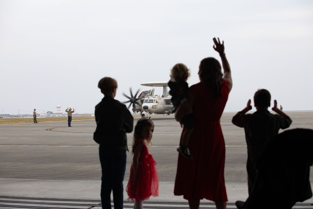 Family members wave to an E-2D Hawkeye aircraft with Airborne Command and Control Squadron (VAW) 125, Carrier Air Wing (CVW) 5, as its taxis on the flightline at Marine Corps Air Station Iwakuni, Japan, Nov. 17, 2024. CVW-5 aircraft and personnel return from being forward-deployed on the USS George Washington providing local air superiority, all-weather offensive air-to-surface attack capabilities, to maintain a free and open Indo-Pacific. (U.S. Marine Corps photo by Cpl. Peter Rawlins)
