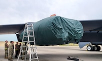People stand around a B-52 Stratofortress that has a covered engine.
