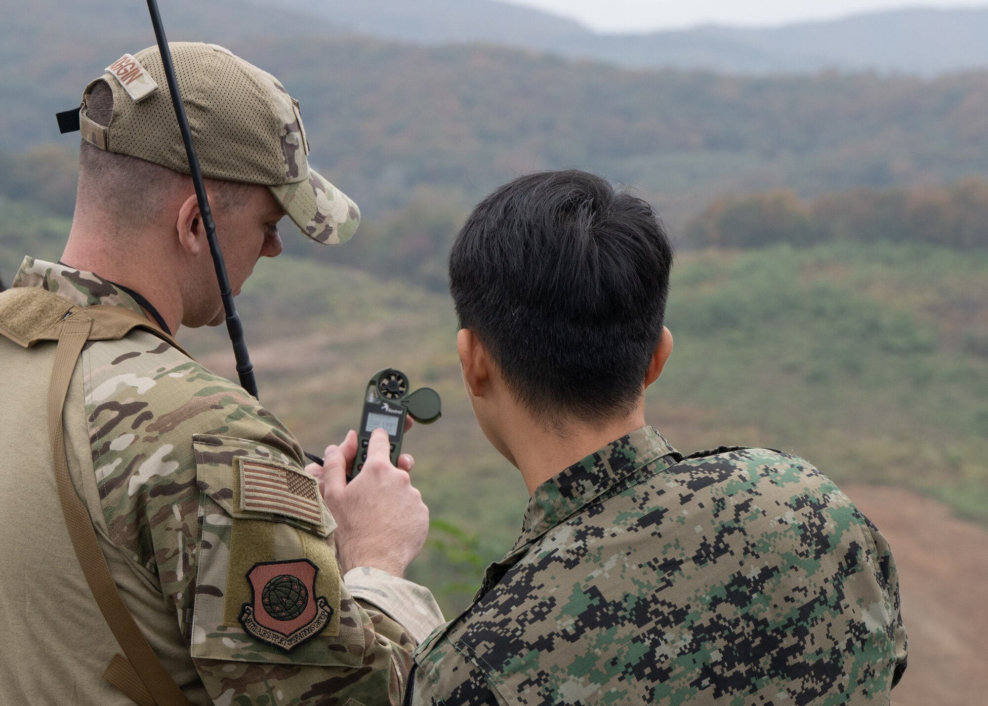 Two uniformed men face away from the camera looking at a weather gage.