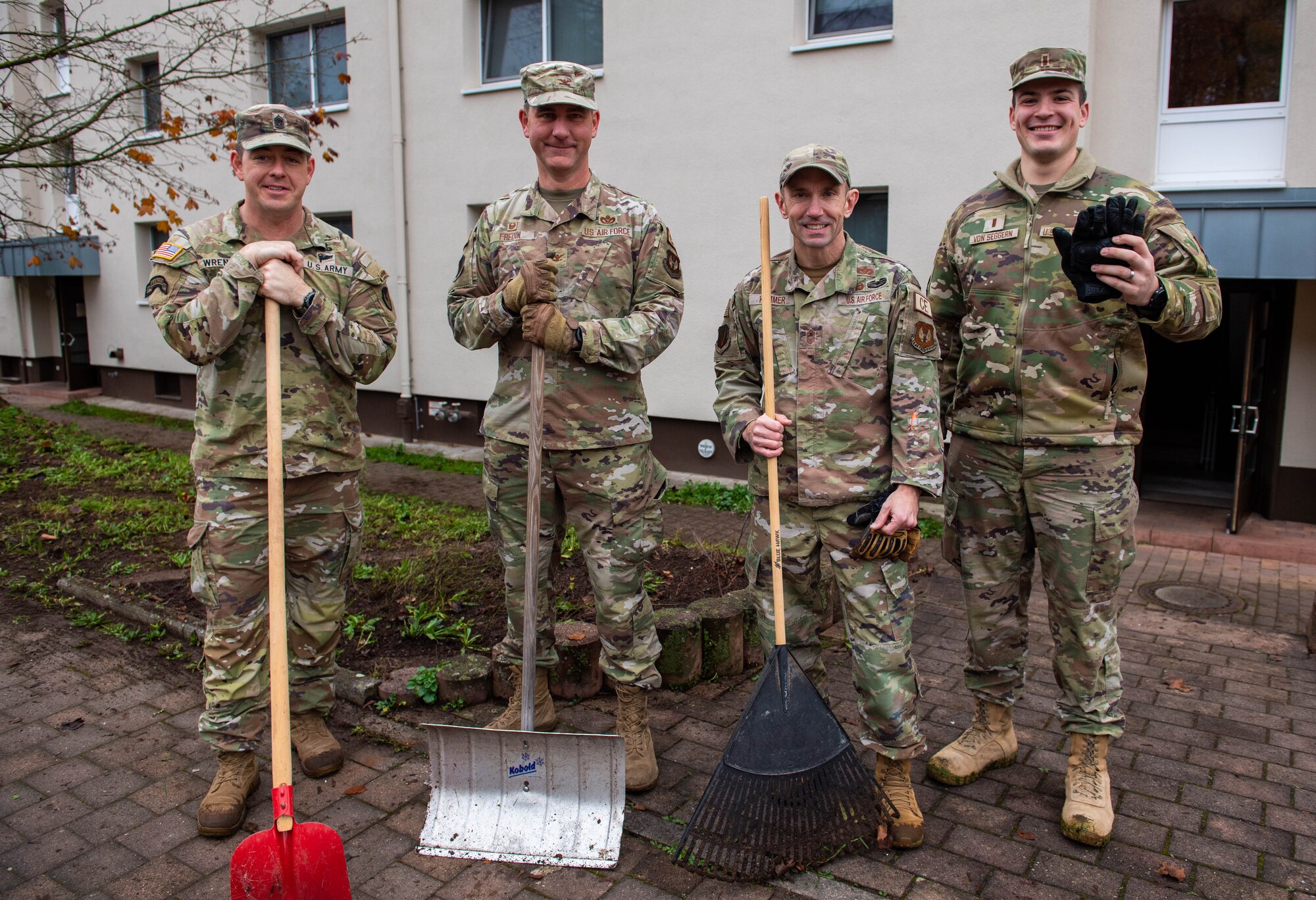 Military members stand for a group photo holding shovels from a clean up on base.