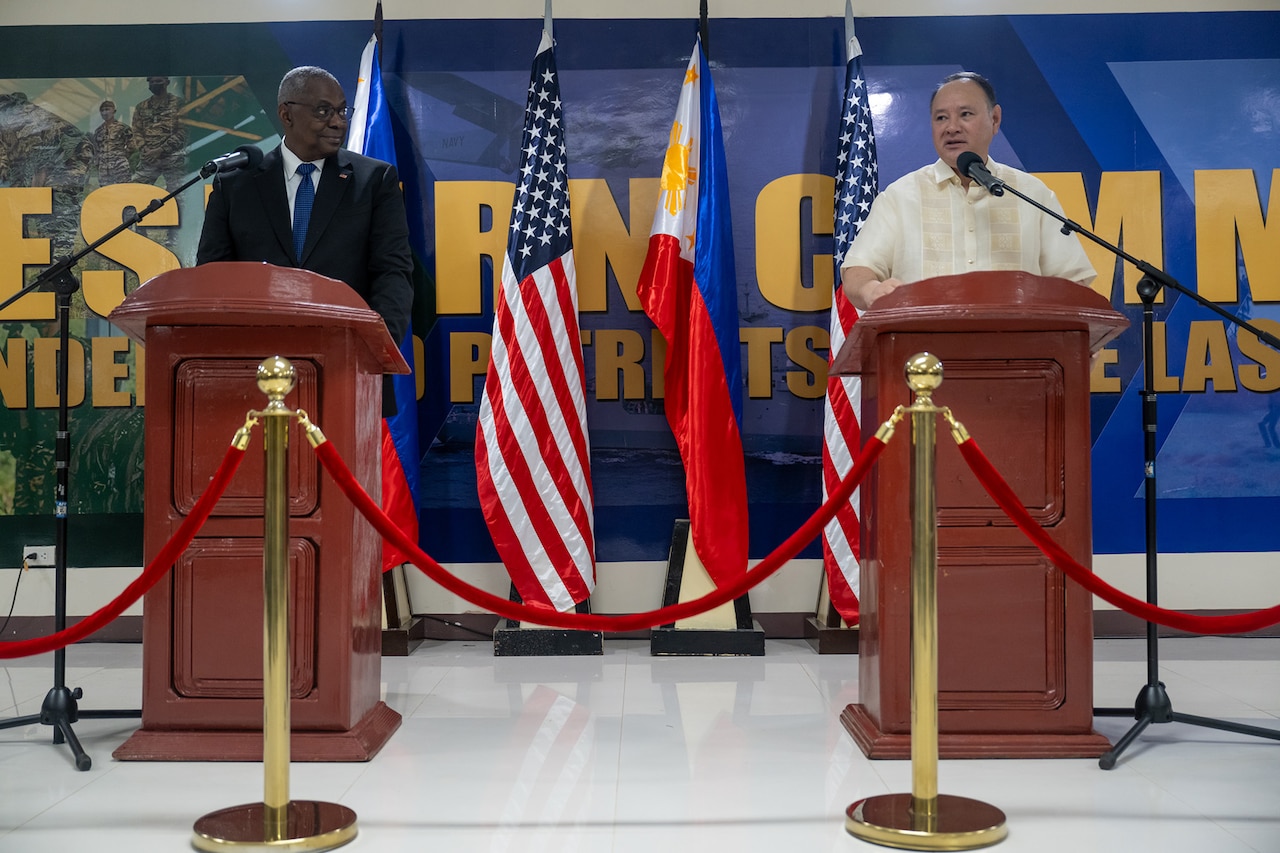 Two civilians stand behind podiums with flags between them.