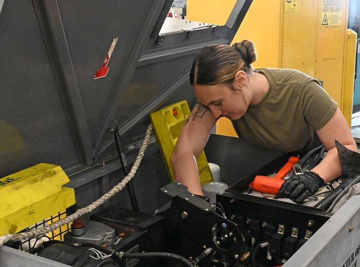 Photo shows woman in uniform reaching into large container with mechanical equipment.