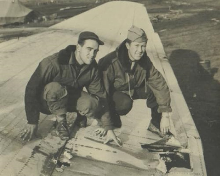 Vintage photo shows two men squatting down on wing of plane