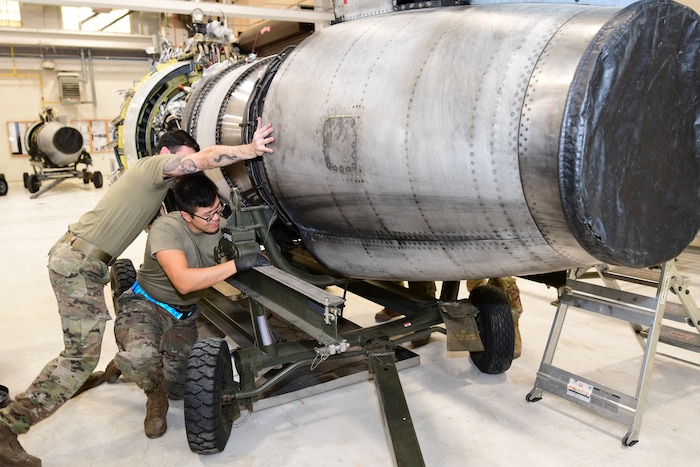 Photo shows two men in military uniforms maneuvering a large aircraft part.