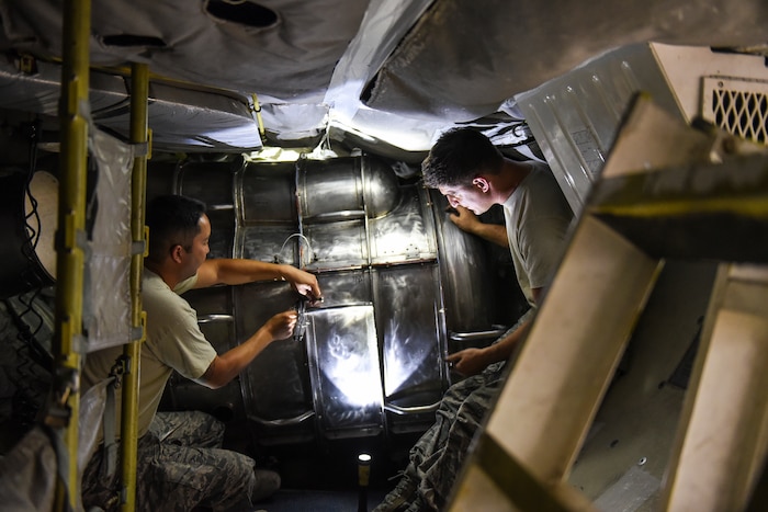 Photo shows two men in uniforms working inside an aircraft removing panels.