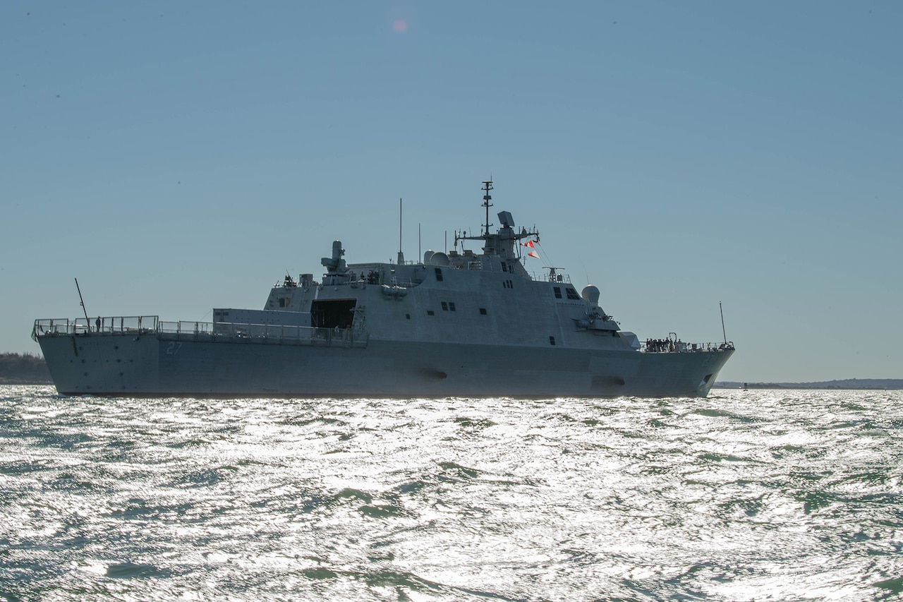 A military ship sails next to a harbor during the day.