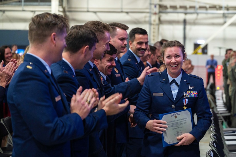 An airman smiles while walking past a group of airmen who are clapping.