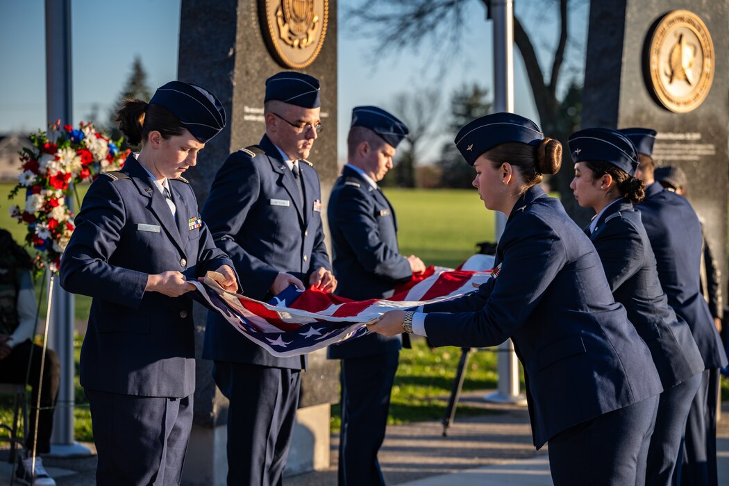 Six high schoolers in Air Force dress uniforms, fold an American flag outdoors