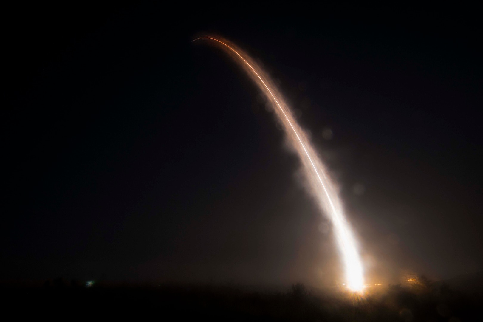 A ballistic missile produces an arc of light against a night sky.