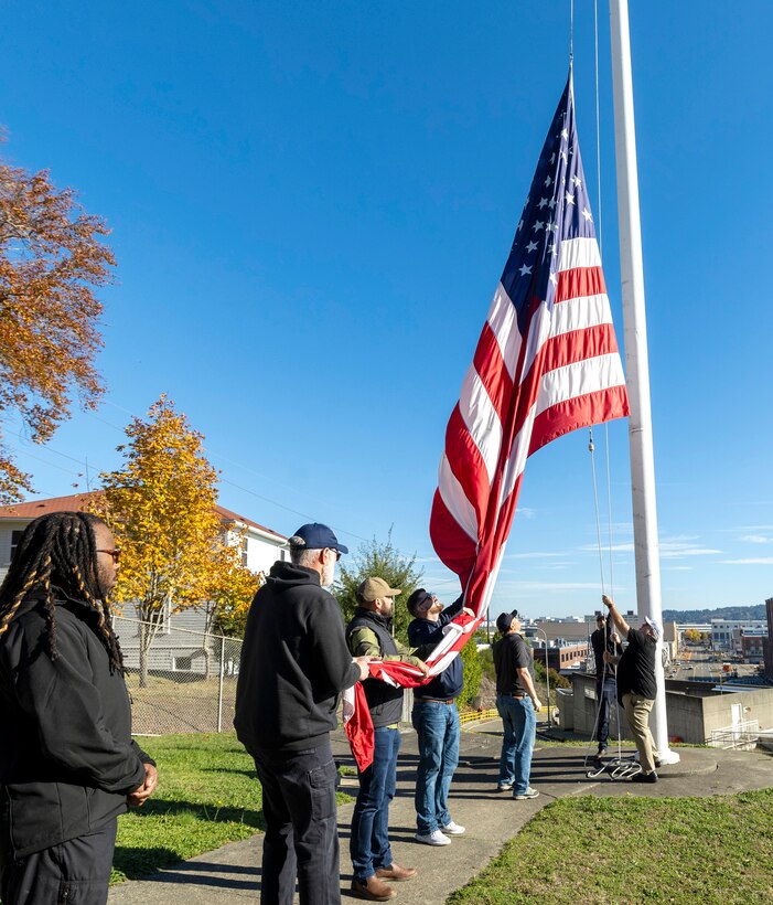 Honor guard members fold the U.S. flag Nov. 7, 2024, during a Veterans Day observance at Puget Sound Naval Shipyard & Intermediate Maintenance Facility in Bremerton, Washington. The event, hosted by the Veterans Employee Resource Group, featured a special flag-folding ceremony at the State Street Gate entrance. (U.S. Navy photo by Wendy Hallmark)