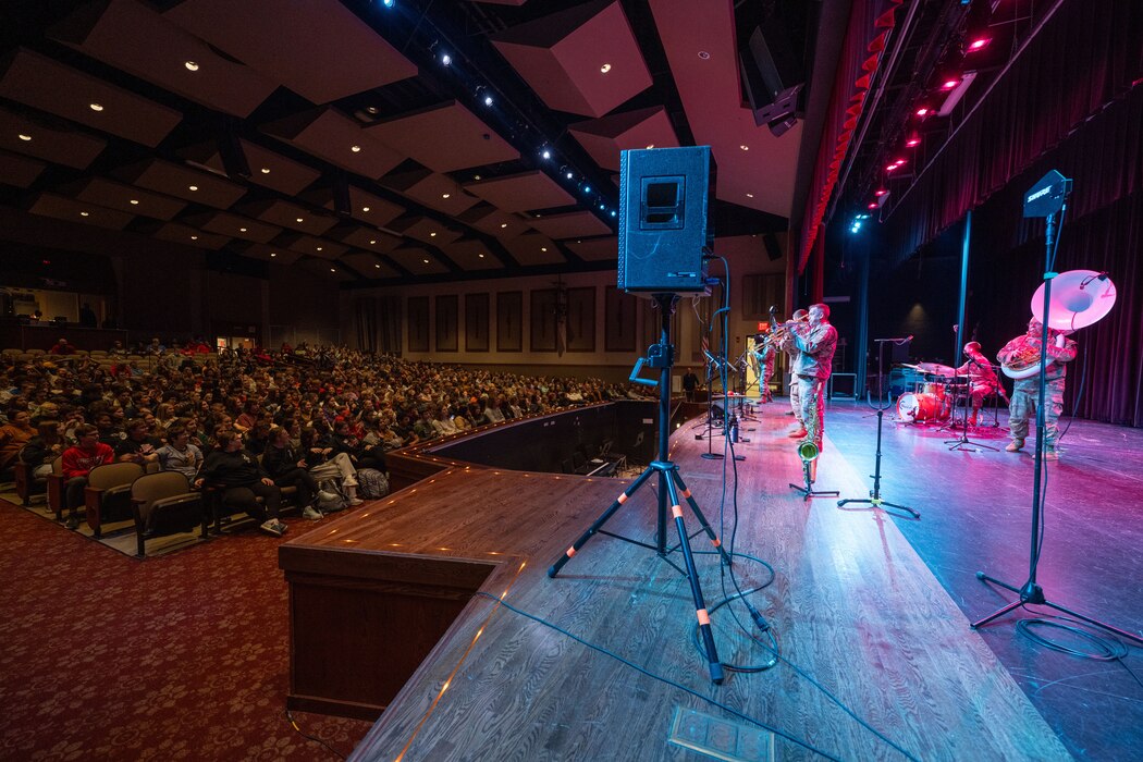 Uniformed band members perform on stage to an audience of students