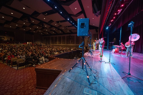 Uniformed band members perform on stage to an audience of students