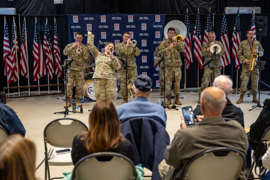 A female uniformed member sings while a brass ensemble performs at a Naval Park.