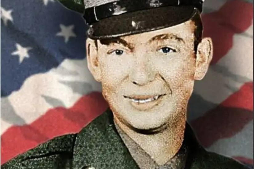 A man in uniform poses for a photo in front of an American flag.