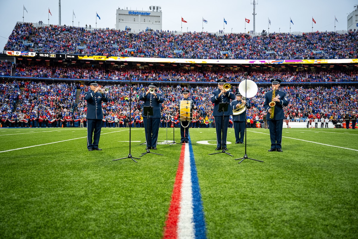 Six brass band members perform a concert on a football field.