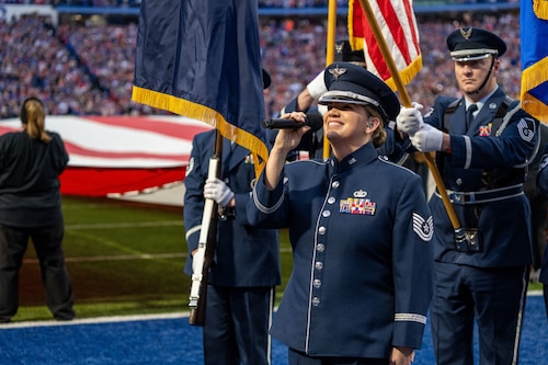 A female uniformed member signs into a microphone on a football field.