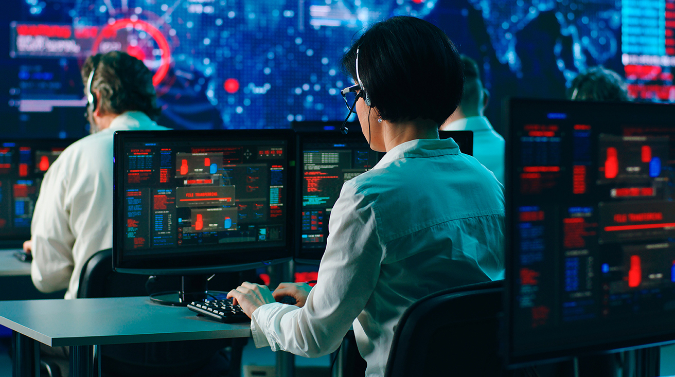 The backs of employees sitting in a data center, wearing headsets, looking at computer screens that show information derived from foreign signals.