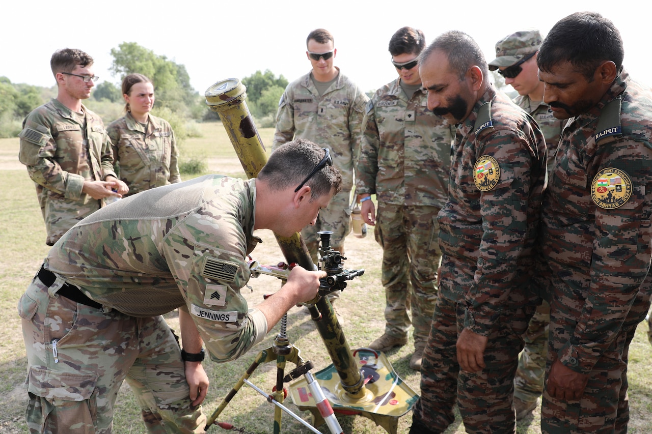 A soldier looks at artillery equipment while among a group of soldiers.