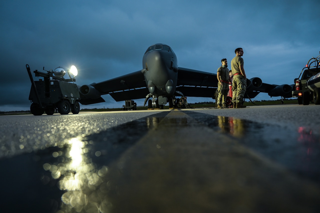 A bomber aircraft sits on the tarmac of an airport during a cloudy night.