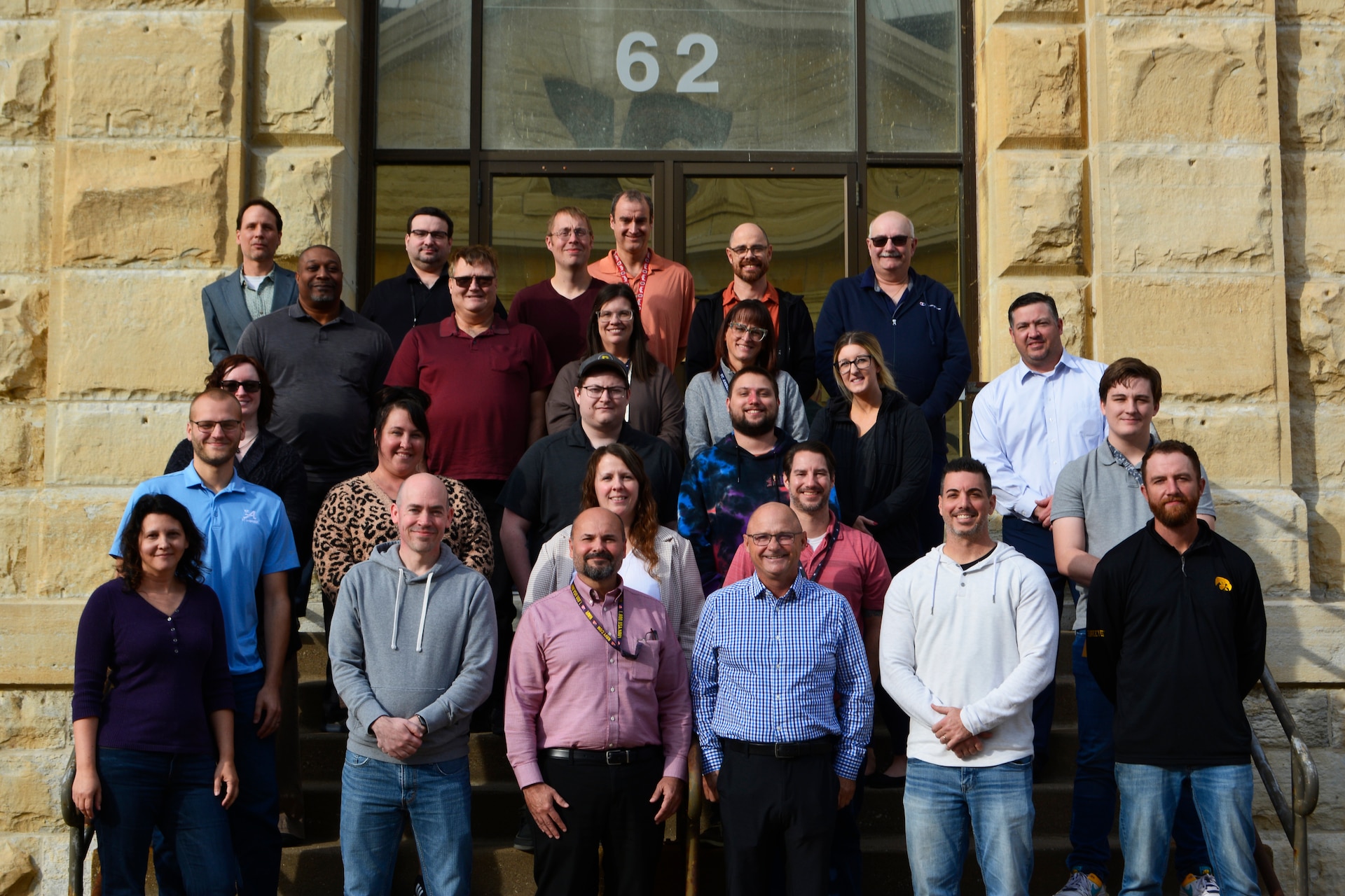 Team of staff stands outside on steps in front of a building