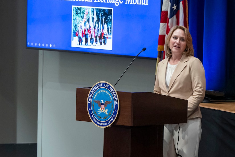 A woman in business attire stands behind a lectern with a 