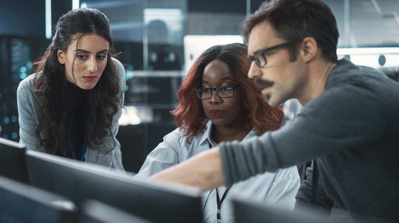 Two females sitting in front of computer screens, talking to a male foreign language advisor.