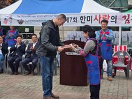 U.S. Army Col. Ryan Workman, U.S. Army Garrison Humphreys commander, presents a certificate of appreciation to Ms. Jang Soon-ok, advisor for the Korean-American Children's Cultural Exchange Association during a kimchi-making festival at Pyeongtaek University, Nov. 16, 2024.