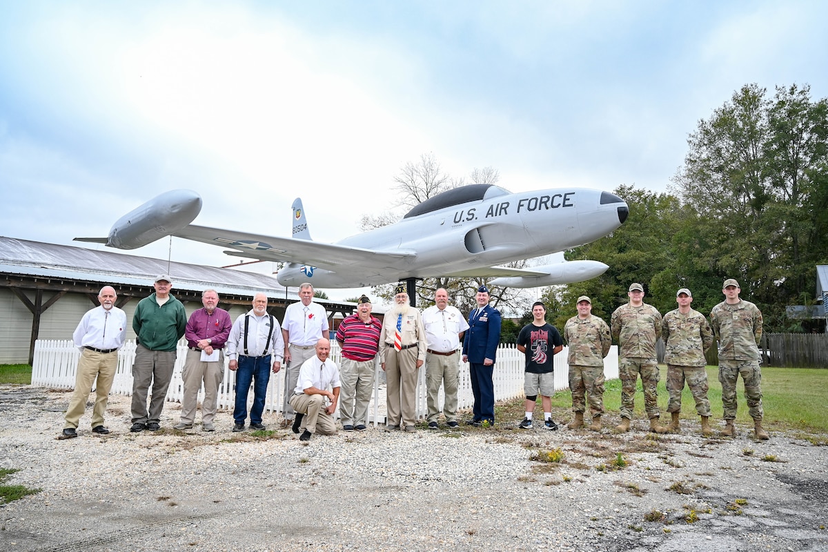 A group of veterans and Airmen pose for a group photo with a T-33.