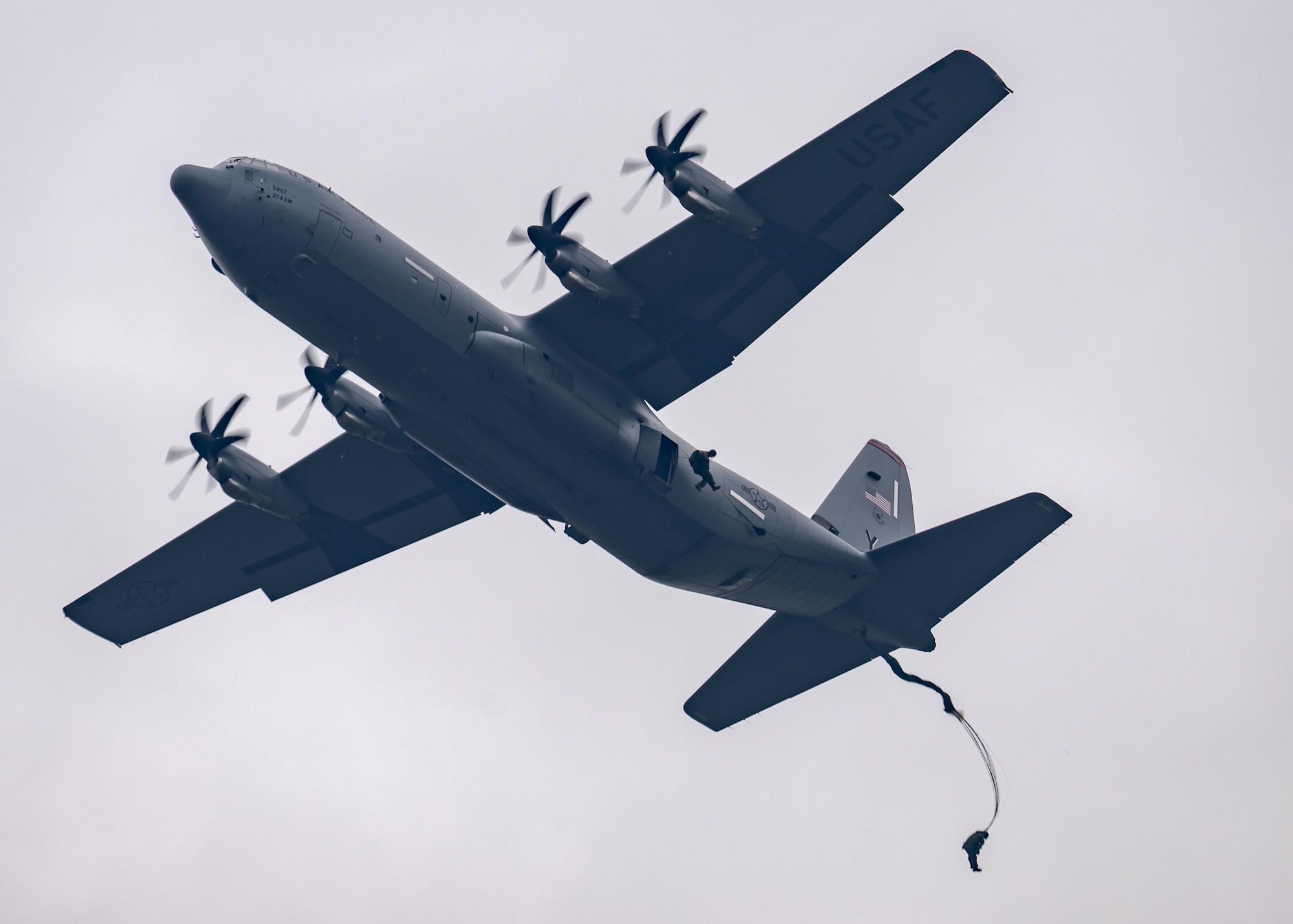 A gray C-130J flies on a gray background.