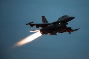 A fighter jet flies from left to right in near darkness.