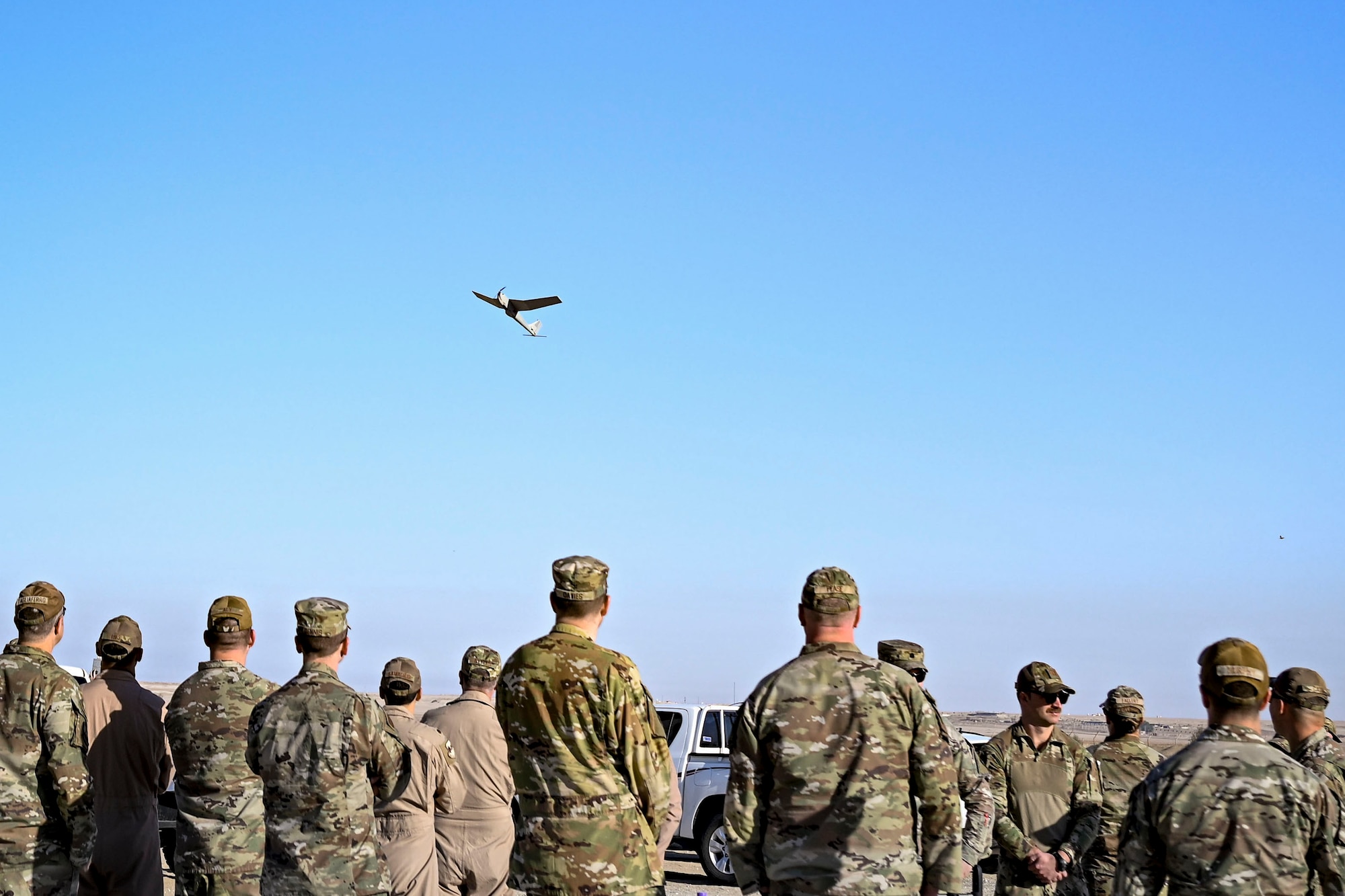 A group of Airmen gather to watch a small unmanned aircraft system (sUAS) fly overhead.
