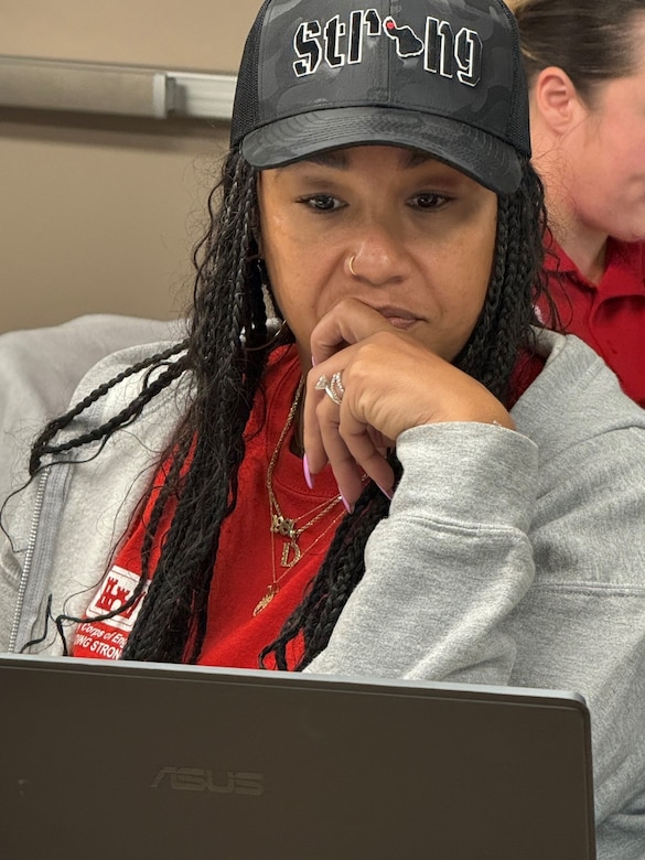 Photo of woman wearing a red USACE Emergency Operations shirt looking at her laptop.