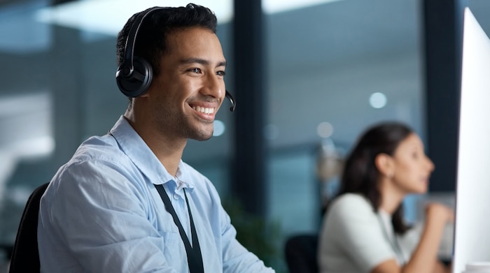 A young man with a headset on working on a computer and sitting next to a woman