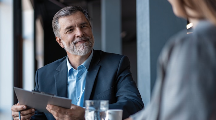 An older white man with a beard speaking to a prospective NSA employee during a clearance interview