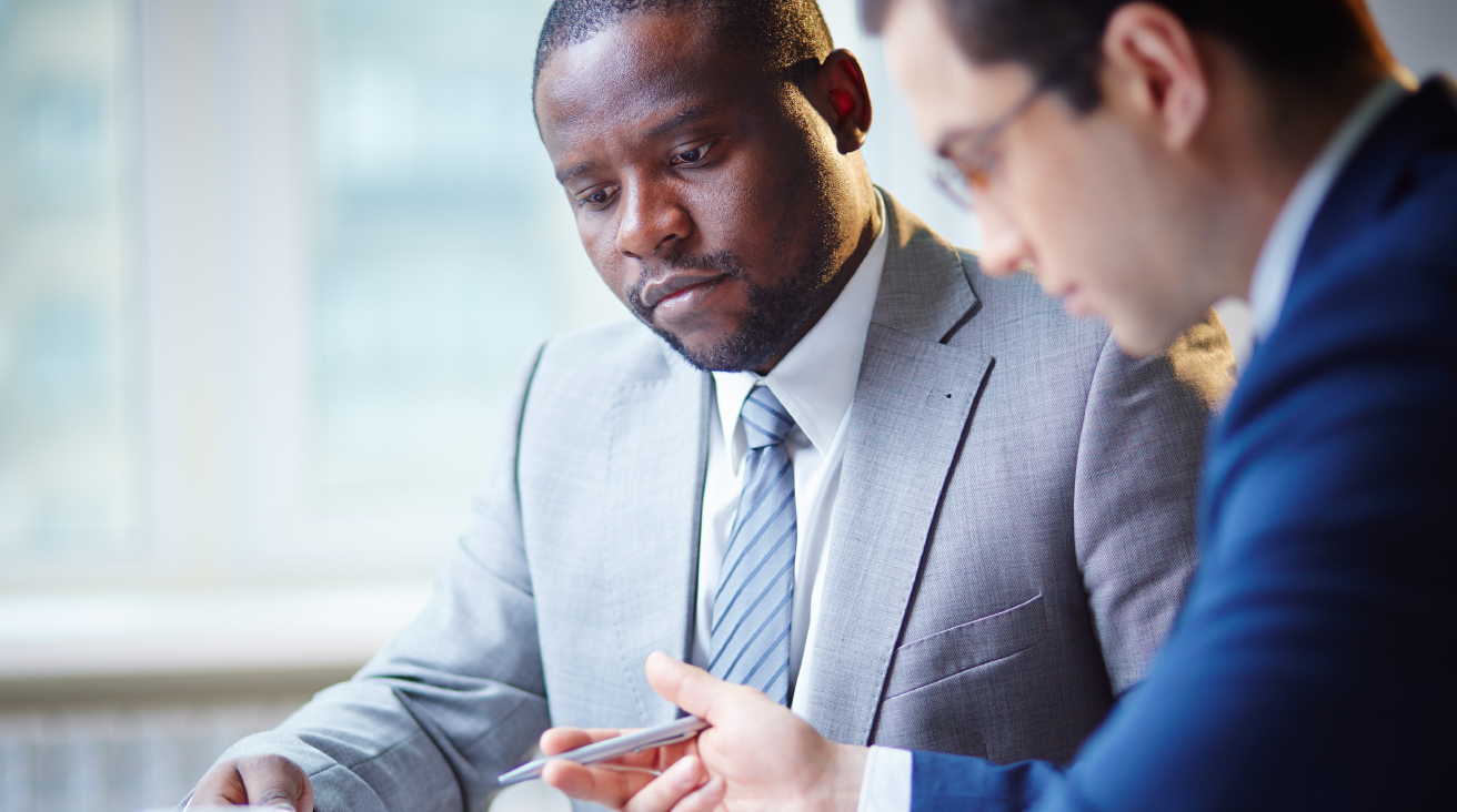 Two men in suits sitting down and analyzing paperwork.