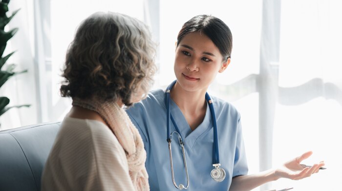 An Asian woman doctor wearing scrubs explaining information to a gray-haired woman next to her