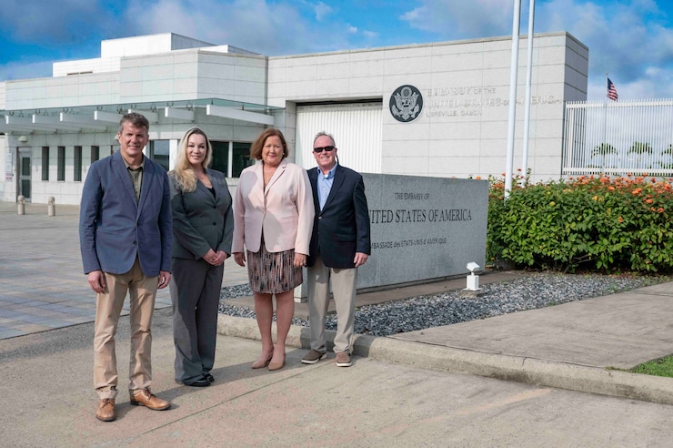 4 people outside a white building, looking at the camera and smiling