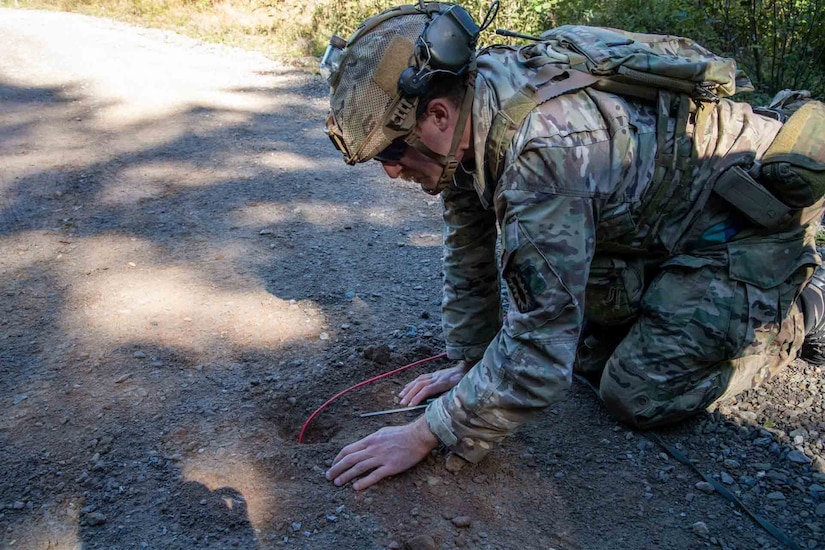 A soldier kneels and scrapes through dirt.