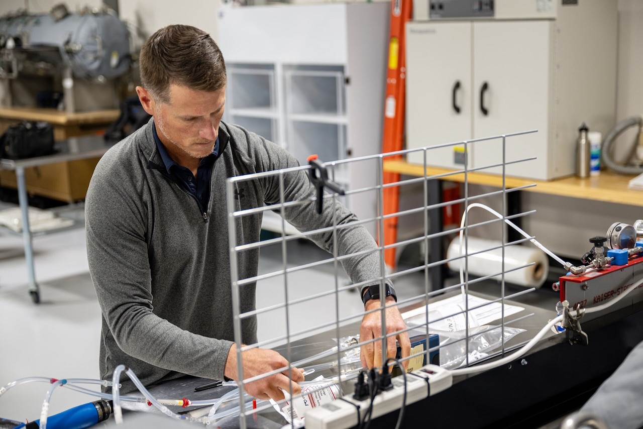 A person adjusts a bag attached to wires at a workstation.