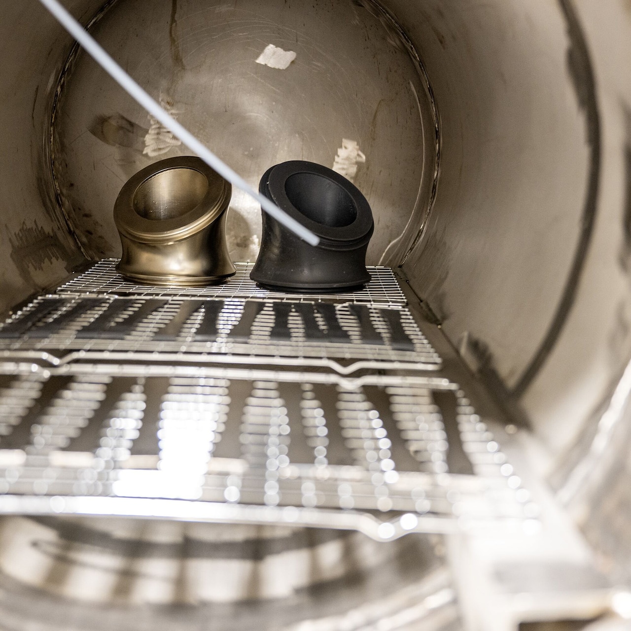 Two tube-like items sit inside a cylindrical metal chamber.