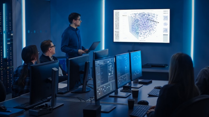 A group of employees sitting in a computer lab with computers in front of them, listening to a presenter