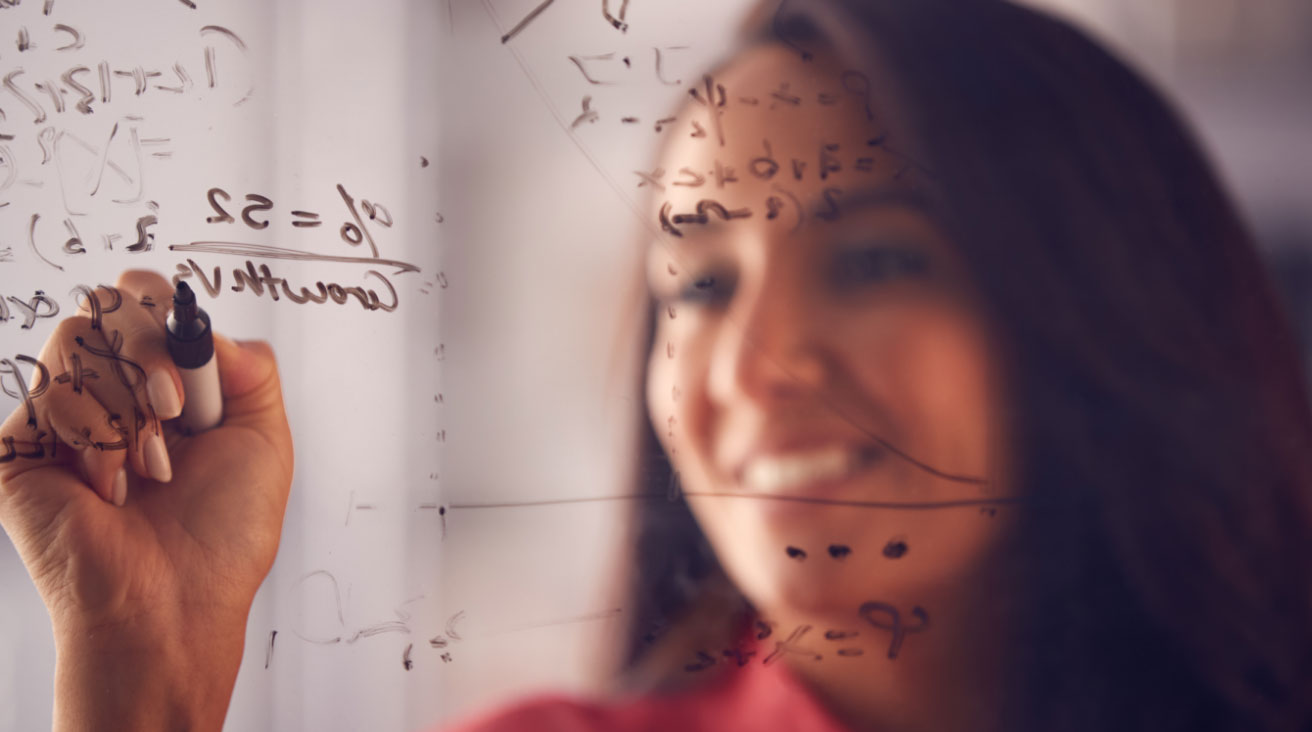 A woman mathematician solving equations on a white board.